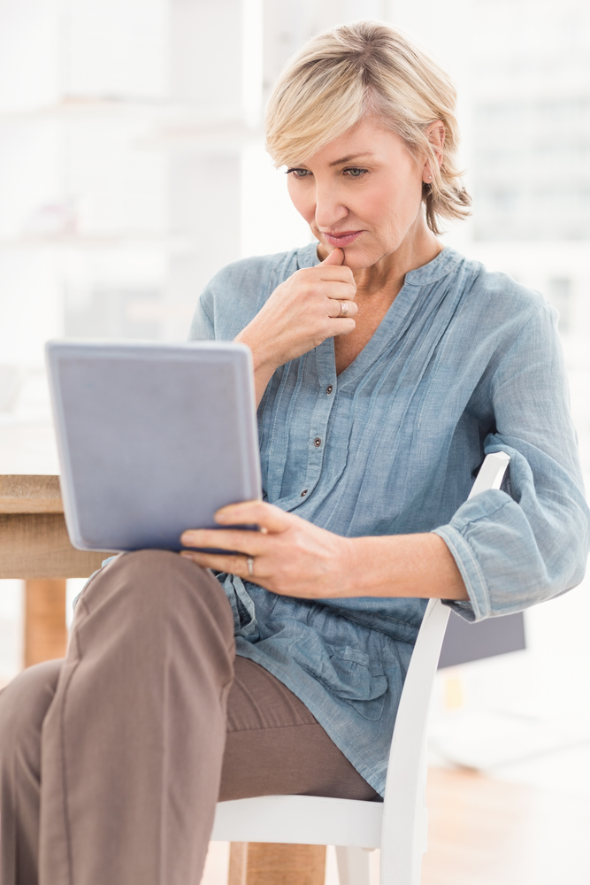 Woman looking at tablet in a chair at an office desk with windows in the background